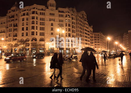 Menschen unter Sonnenschirmen an einem regnerischen Abend auf den Straßen von Valencia in Spanien Stockfoto