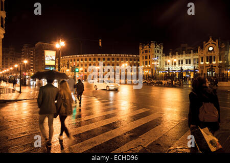 Menschen unter Sonnenschirmen an einem regnerischen Abend auf den Straßen von Valencia in Spanien auf einem Fußgängerüberweg Stockfoto