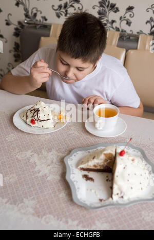 Junge trinkt Tee mit Kuchen am Tisch Stockfoto