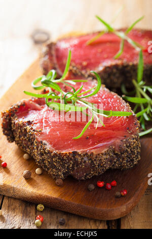 rohes Rindersteak mit Gewürzen und Rosmarin auf hölzernen Hintergrund Stockfoto