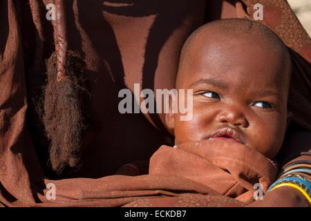 Namibia, Kunene Region, Kaokoland, Himba-Dorf in der Nähe von Opuwo, Himba Kind in den Armen seiner Mutter Stockfoto