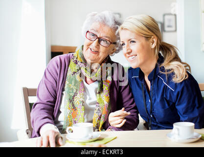 Glücklich weibliche Hausmeister und senior Frau wegsehen sitzend am Tisch im Pflegeheim Stockfoto