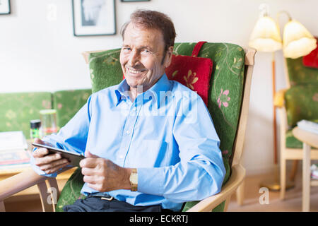 Porträt von senior glücklich halten digital-Tablette und sitzt auf Sessel im Pflegeheim Stockfoto