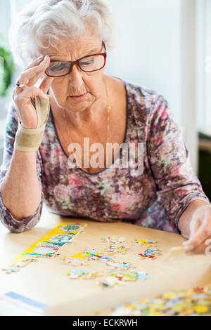 Ältere Frau Lösung Puzzle am Tisch im Pflegeheim Stockfoto