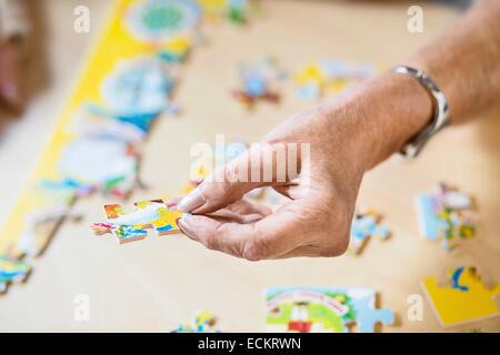 Zugeschnittenes Bild der senior Frau Hand hält Puzzleteil am Tisch im Pflegeheim Stockfoto