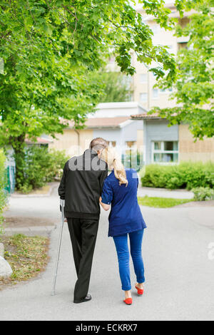 Voller Länge Rückansicht der liebevolle weibliche Hausmeister und behinderten älteren Mann zu Fuß auf Straße Stockfoto