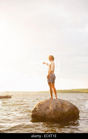 Voller Länge Seitenansicht der Mann zeigte auf Felsen im See gegen Himmel stehend Stockfoto