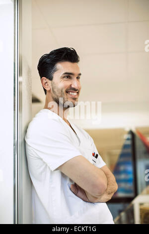 Lächelnden jungen männlichen Arzt stützte sich auf Wand im Krankenhaus Stockfoto