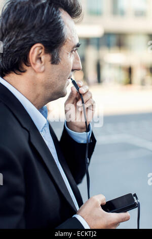 Seitenansicht der Geschäftsmann kommunizieren über Kopfhörer mit Handy auf Straße Stockfoto