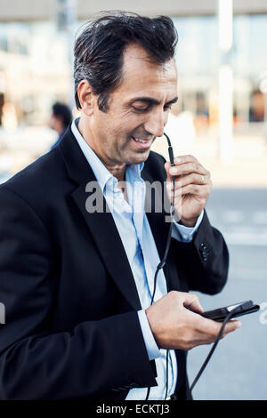 Geschäftsmann, die Kommunikation über Kopfhörer bei der Verwendung von Handy auf Straße Stockfoto