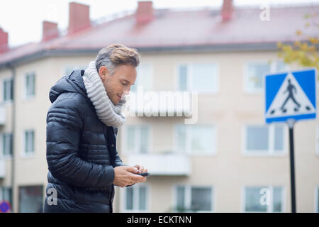 Reifer Mann mit Smartphone gegen Gebäude Stockfoto