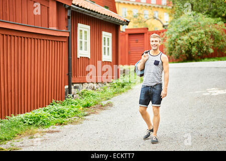 Lächelnder junge Mann gehen auf der Straße gegen Haus Stockfoto