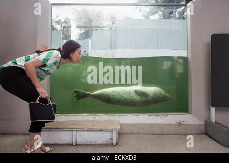 Eine Frau, die durch ein Marinebehälter in ein Aquarium Ausstellung hocken.  Ein Tier im Wasser. Stockfoto