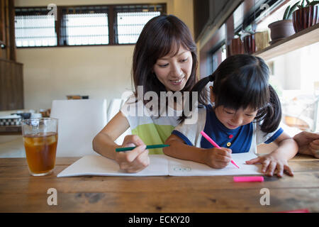Mutter und Tochter sitzen an einem Tisch, zeichnen mit Filzstift Stifte, lächelnd. Stockfoto
