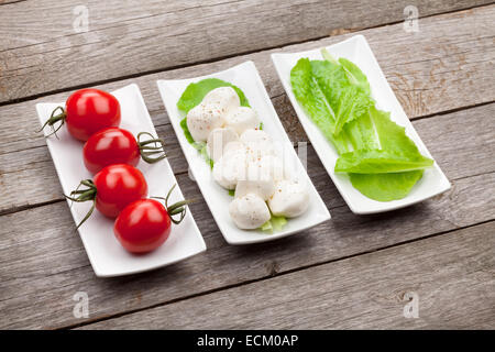 Tomaten, Mozzarella und grünem Salat Blätter auf Holztisch Hintergrund Stockfoto