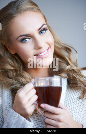 Attraktive Frau lächelnd mit schönen langen lockigen blonden Haaren, eine Tasse Kaffee zu genießen, wie sie die Kamera mit einem freundlichen s sieht