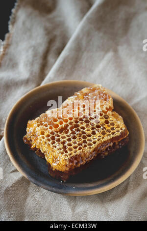 Bienenwabe auf Keramikplatte über alten Holztisch. Stockfoto