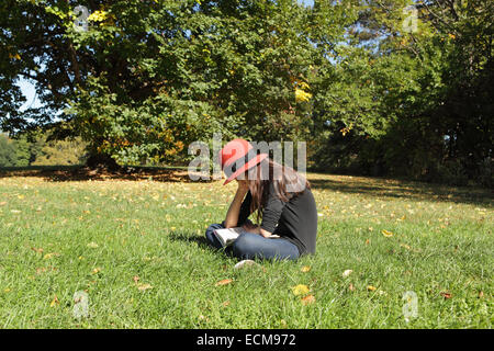 Junges Mädchen ein Buch auf der Wiese unter einem Baum in einem Sommerpark in Brooklyn Stockfoto