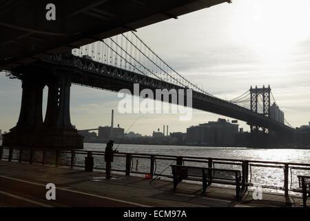 Mann Angeln von der Esplanade East River in New York City, wie die Sonne über die Manhattan Bridge Stockfoto