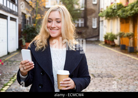 junge Frau, die ihre Nachrichten mit einem Kaffee Stockfoto