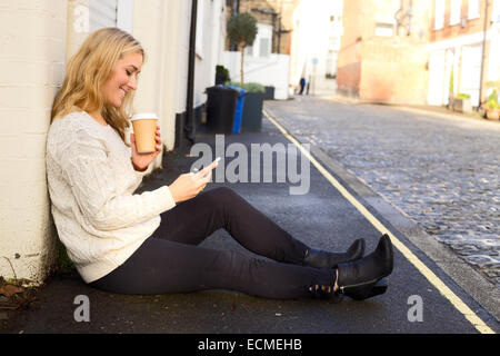 junge Frau überprüft ihr Telefon mit einem Kaffee Stockfoto