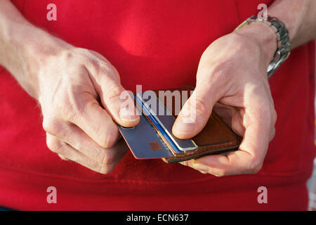 Ein Mann im roten Pullover entfernen eine Visa-Kreditkarte aus einer Brieftasche für einen Kauf zu bezahlen. England, UK, Großbritannien Stockfoto