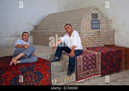 Zwei usbekische Männer entspannend auf Teppichen in einer alten historischen Karawanserei, in der historischen Mitte von Bukhara / Buxoro, Usbekistan Stockfoto