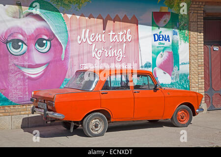 Alte orange Trabant parkte vor Werbung an Wand in Usbekistan gemalt Stockfoto