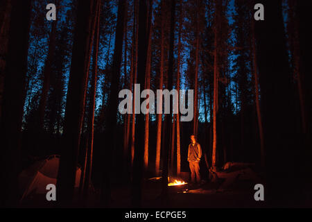 Ein Mann steht am Lagerfeuer umgeben von Lodgepole Pine an Jonas Creek Campground in Jasper Nationalpark in den Rocky Mountains Stockfoto