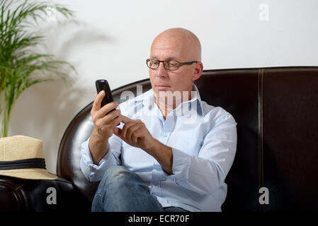 ein Senior sitzen in einem Sofa und einem Telefon Stockfoto