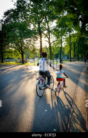 Mutter und Kind Radfahren in einer Stadt park Vondelpark Amsterdam an einem sommerlichen Abend Stockfoto