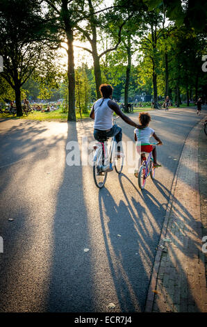 Mutter und Kind Radfahren in einer Stadt park Vondelpark Amsterdam an einem sommerlichen Abend Stockfoto