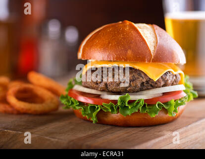 Ein köstliches Gourmet-Cheeseburger auf einem Brezel-Brötchen mit Salat, Zwiebel und Tomate. Stockfoto