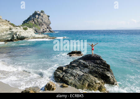 Frau am Strand oben auf Felsen vor Mamma Mia Kapelle Agios Ioannis, Skopelos, Griechenland. Oktober. Stockfoto