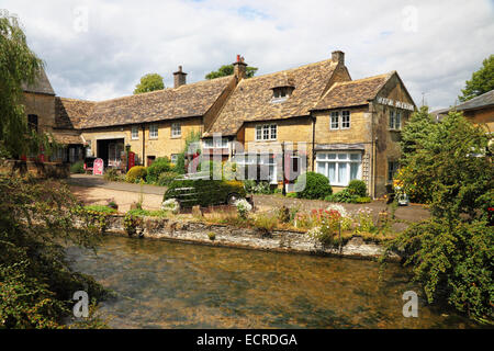 Eine Reihe von Cotswold Steinhütten durch einen Bach mit einem Motor Museum-Schild. Stockfoto