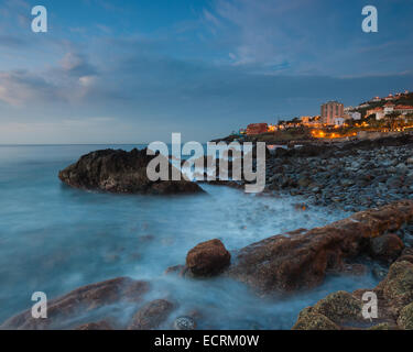 Trübe Wasser am Ufer bei Sonnenuntergang mit einer Stadt im Hintergrund Stockfoto