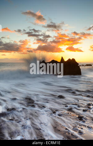 Wellen, die gegen einen Felsen im Meer bei Sonnenuntergang Stockfoto