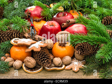 Äpfel, Mandarin Früchten, Walnüssen, Cookies und Gewürzen mit Weihnachtsbaum-Niederlassungen. Festliches Essen Hintergrund Stockfoto