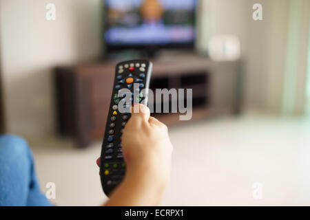 Über die Schulter-Blick des Mädchens auf Sofa sitzen halten tv remote und Surfen Programme im Fernsehen Stockfoto