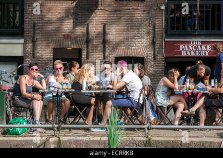 Amsterdam-Pfannkuchen-Bäckerei-Restaurant am Prinsengracht Kanal. Leute sitzen auf dem Rand des Wassers. Aus dem Kanal zu sehen. Stockfoto