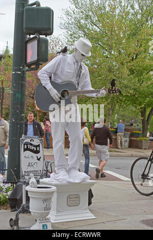 Mann in weiß, eine lebende Statue ganz in weiß gekleidet mit Krähen thront auf ihm spielt Gitarre für Tipps in Asheville, NC Stockfoto