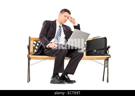 Verärgert Geschäftsmann arbeiten auf einem Laptop sitzt auf einer Bank, die isoliert auf weißem Hintergrund Stockfoto