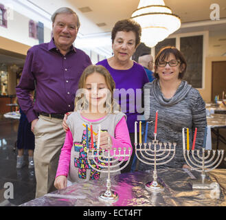 Merrick, New York, USA. 18. Dezember 2014. Enkelin EMILY MIKOLA, 8, ihr Opa und Oma BLOOMFIELD, und (ganz rechts) ihren Freund MARCI SILVERMAN, jeder bekommen eine Menora bereit wenn Merrick jüdisches Zentrum Attemps wieder den Guinness Weltrekord für die meisten Menorot beleuchtet in einem gleichzeitig platzieren, die die Gemeinde 2011 stattfinden. In der dritten Nacht von Hanukkah ebenfalls das "Light Up the Night 2 - bringt die Rekord-Haus" Ereignis eine feierliche Kerze Beleuchtung in das wichtigste Heiligtum. Obwohl die Menorah Beleuchtung Ziel mindestens 1.000 Menorot Licht verpasst wurde, und der Datensatz w Stockfoto