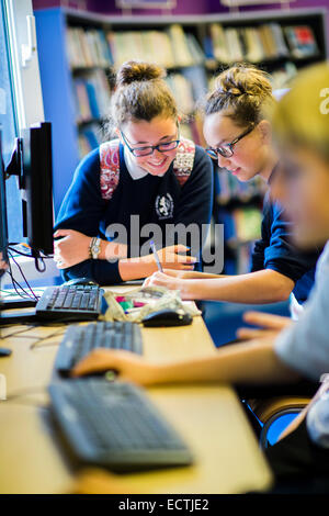 Höhere Schulbildung Wales UK: zwei Mädchen im Teenageralter lesen und arbeiten auf einem Computer in der Schulbibliothek während ihrer Mittagspause Stockfoto