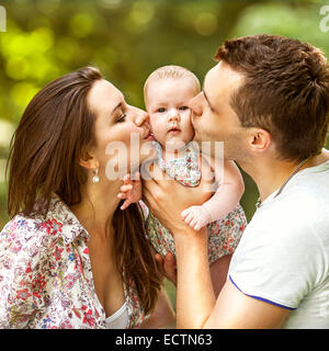 glückliche Mutter und Vater küssen seine kleine Tochter im park Stockfoto