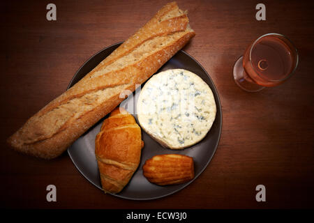 Französischer Blauschimmelkäse, Baguette, Croissant, Madeleine und Glas Wein auf dem Tisch Stockfoto