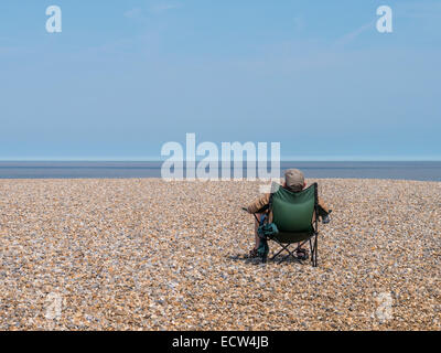 Eine einsame Figur genießt die Frühlingssonne am Strand von Aldeburgh, Suffolk. Stockfoto