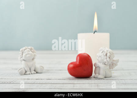 Statuetten von kleinen Engeln mit steinernen Herzen und Kerzen auf hellem Hintergrund Stockfoto