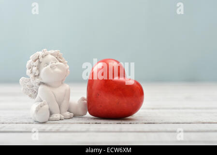 Statuetten von kleinen Engeln mit steinernen Herzen auf hellem Hintergrund Stockfoto