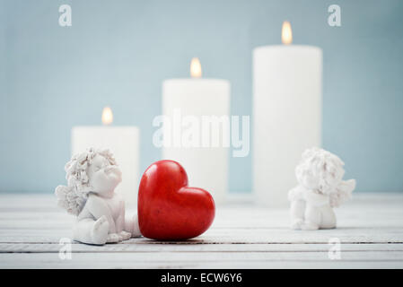Statuetten von kleinen Engeln mit steinernen Herzen und Kerzen auf hellem Hintergrund Stockfoto